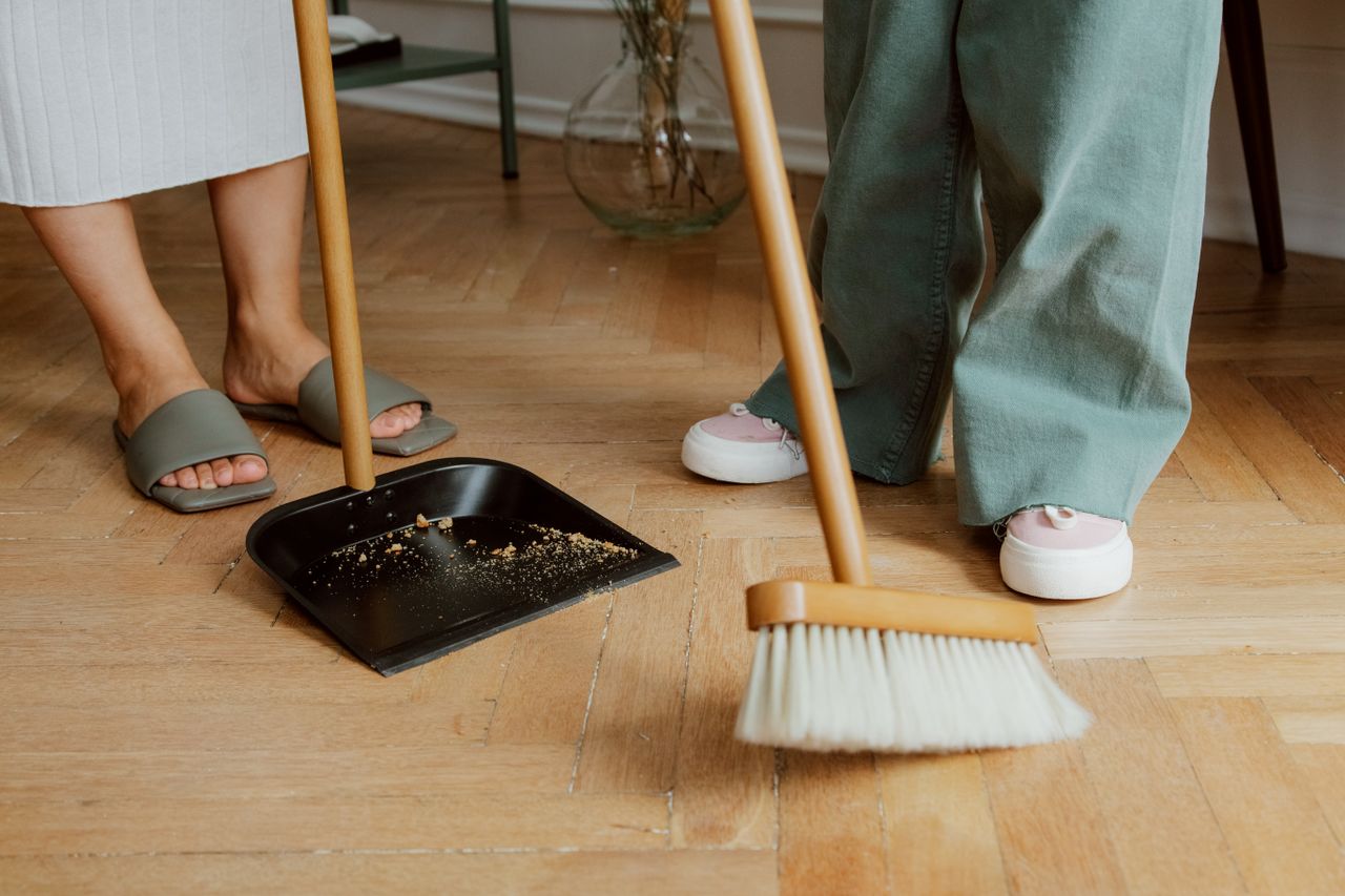 why-choose-us Close-up of people cleaning wooden floor with broom and dustpan indoors.