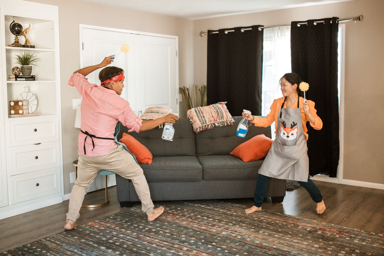 core-values A joyful couple engages in a playful cleaning fight in their living room, showcasing light-hearted domestic life.
